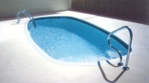The Caladesi pool in a light concrete deck, with a chrome handrail at each end and a dark tile band along the waterline.