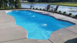 The Costa Rica pool with bright blue water in a concrete deck, with two water jets and chairs by a lake.